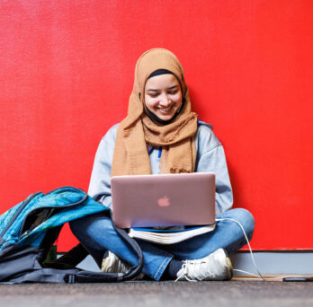 Undergraduate student studying online in front of red wall 