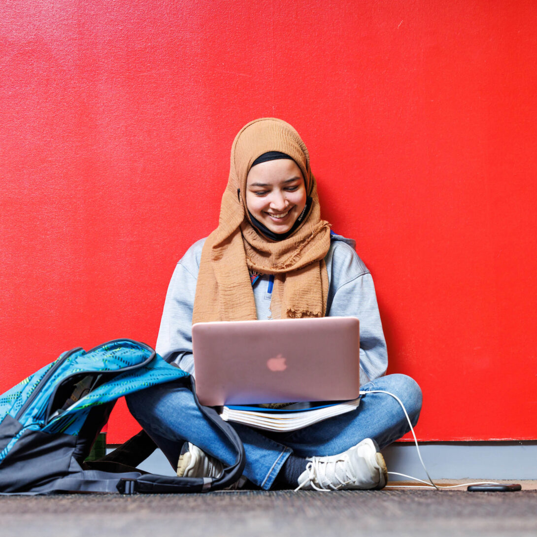 Undergraduate student studying online in front of red wall
